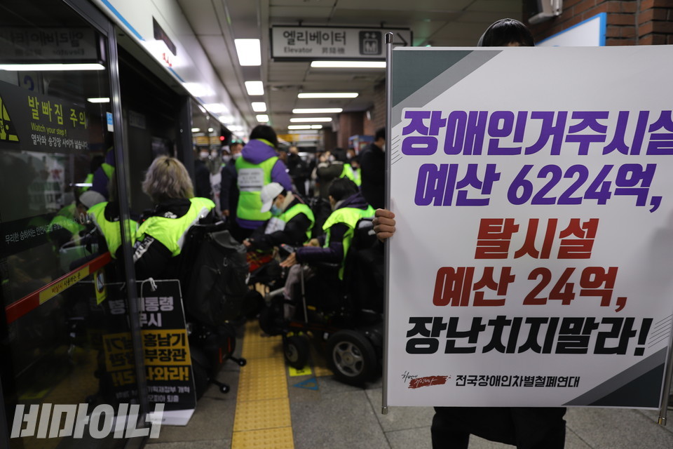 성신여대입구역에서 한 활동가가 '장애인거주시설 예산 6224억, 탈시설 예산 24억 장난치지 말라'라는 현수막을 들고 있다. 뒤로 지하철이 멈춰 서 있다. 사진 허현덕
