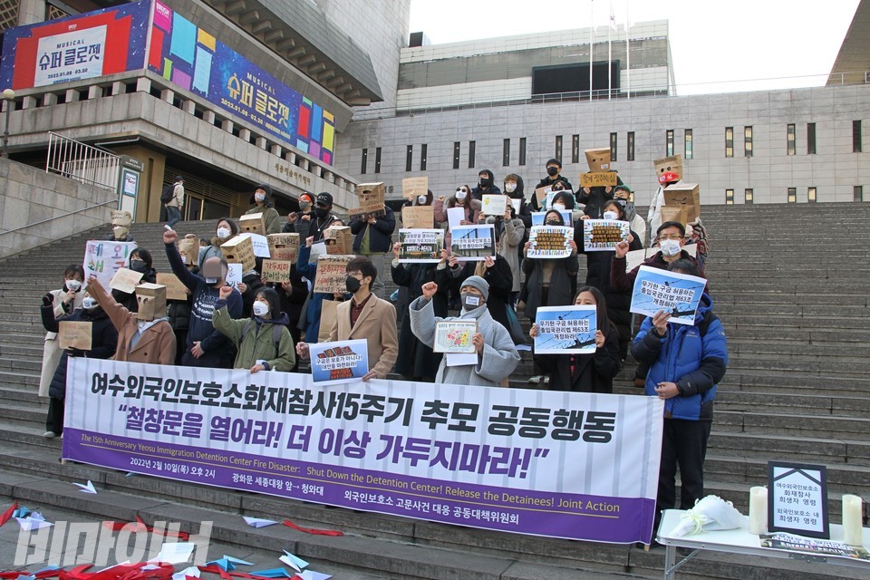 기자회견 현장. 현수막에 ‘여수외국인보호소 화재참사 15주기 추모 공동행동, 철창문을 열어라! 더는 가두지 마라!’라고 적혀 있다. 참가자는 다양한 피켓과 봉투가면을 준비했다. 자유를 상징하는 종이비행기를 날리고 ‘투쟁’을 외치고 있다. 사진 하민지