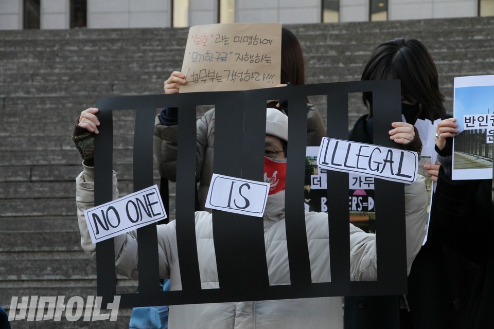 한 활동가가 있다. 검은색 쇠창살을 재현한 피켓을 들고 있다. 피켓에는 “불법으로 존재하는 사람은 없다(No one is illegal)”고 젹혀 있다. 사진 하민지