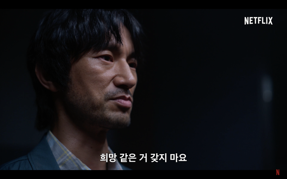 한 인물의 굳은 표정이 검은 배경에 크게 담긴다. 눈썹을 살짝 가리고 뒷목을 덮는 길이의 머리카락, 짧게 남아 있는 수염, 탁한 상의. “희망 같은 거 갖지 마요”라는 자막. 넷플릭스 시리즈 〈지금 우리 학교는〉 예고편 화면 캡쳐.