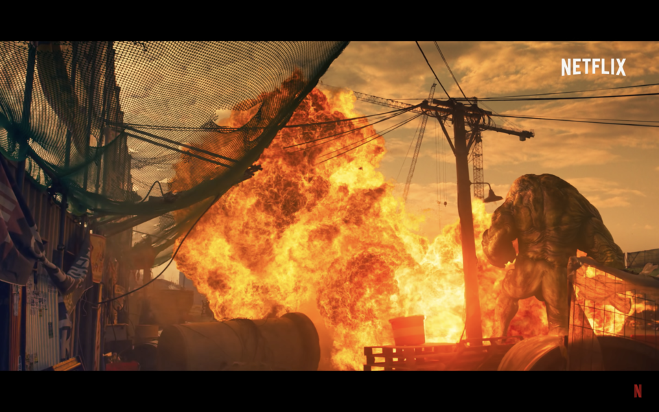 해가 저무는 초저녁, 찢어진 그물망과 현수막들이 지저분하게 걸린 공사장. 크레인 근처에서 높고 커다란 불길이 터져 나오고, 크레인 높이에 약간 못 미치는 거대한 근육질의 괴물이 불길에 움찔한다. 넷플릭스 시리즈 〈스위트 홈〉 예고편 화면 캡쳐.