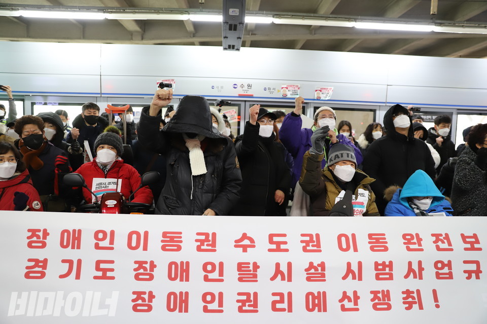 수원역 기자회견 현장. 현수막에 ‘장애인 이동권 수도권 이동 완전 보장, 경기도 장애인 탈시설 시범사업 규탄, 장애인권리예산 쟁취!’라고 적혀 있다. 활동가들이 ‘투쟁’을 외치고 있다. 사진 하민지