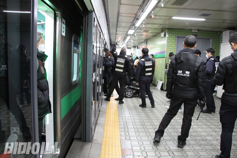 지하철이 멈춰 서 있고 한 시민이 문 앞에 서 있다. 지하철보안관과 경찰이 장애인 활동가를 둘러싸고 있다. 사진 허현덕