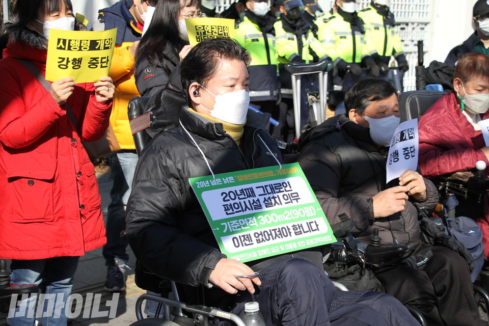 기자회견에 참가한 최용기 한국장애인자립생활센터협의회 대표의 목에 피켓이 걸려 있다. 피켓에는 ‘20년째 그대로인 편의시설 설치 의무 이젠 없어져야 합니다’라고 적혀 있다. 사진 이슬하