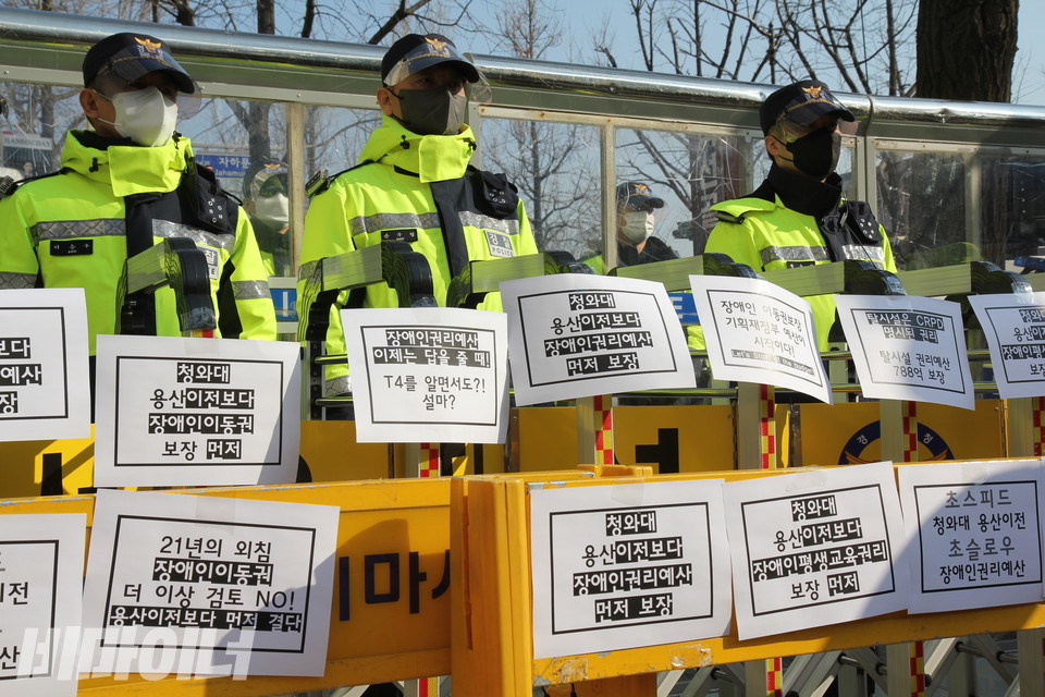 경찰 앞에 쳐진 바리케이드에 종이들이 덕지덕지 붙어 있다. 종이에는 “청와대 용산 이전보다 장애인권리예산 먼저 보장”, “21년의 외침 장애인 이동권 더 이상 검토 NO! 용산 이전보다 먼저 결단” 등의 문구가 적혀 있다. 사진 이슬하
