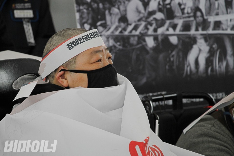 차한선 회원의 눈에 눈물이 맺혀 있다. 그의 뒤로 2002년 이동권 투쟁 사진이 보인다. 사진 하민지