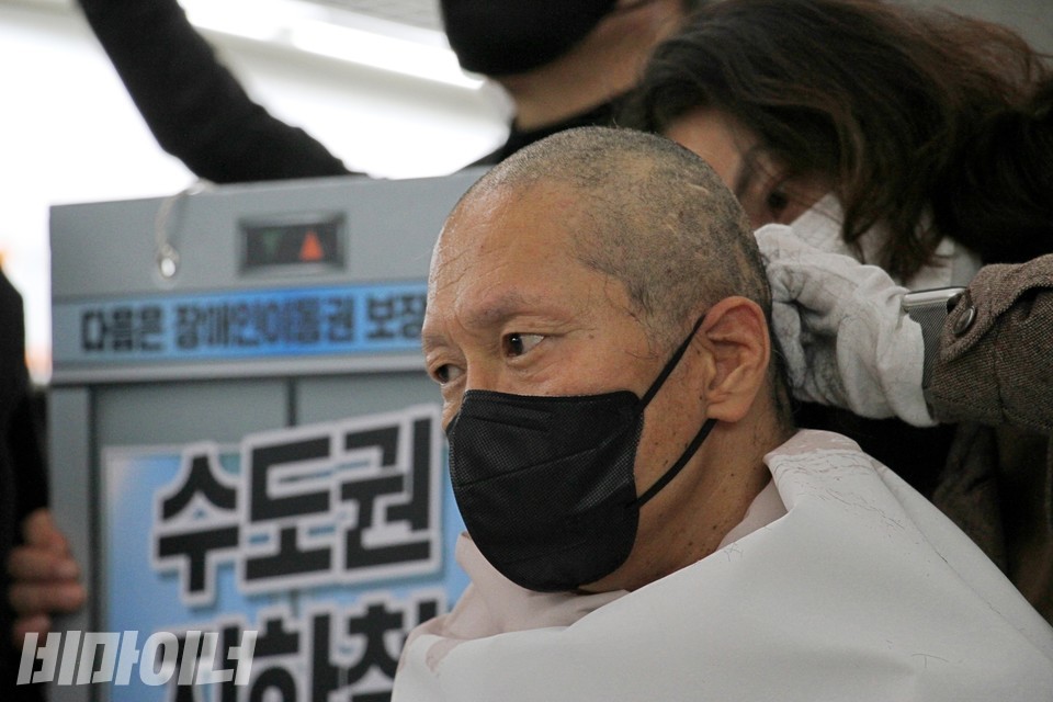 삭발 중인 김태현 사무국장. 그의 뒤에 ‘장애인 이동권 보장, 수도권 지하철’이라고 적힌 피켓이 있다. 사진 이슬하