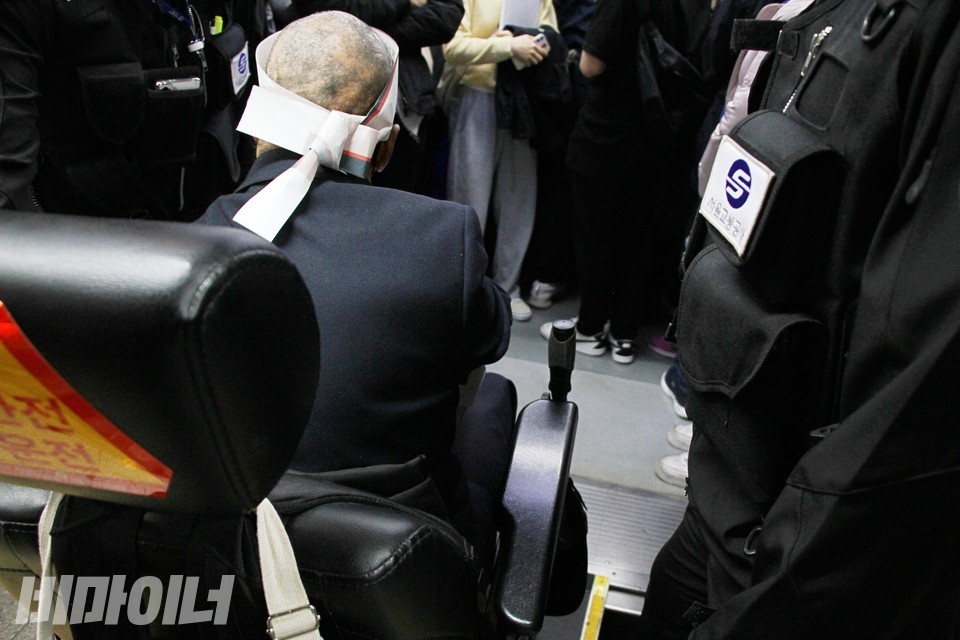 김태현 사무국장이 지하철에 타고 있다. 김 사무국장이 탈 비좁은 공간 뒤로 비장애인 승객들의 발이 보인다. 오른쪽엔 서울교통공사 직원이 있다. 사진 이슬하