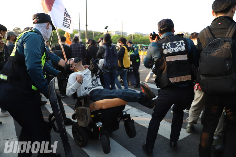 경찰이 휠체어를 뒤에서 끌어당겨 활동가의 몸이 뒤로 넘어가고 있다. 사진 강혜민