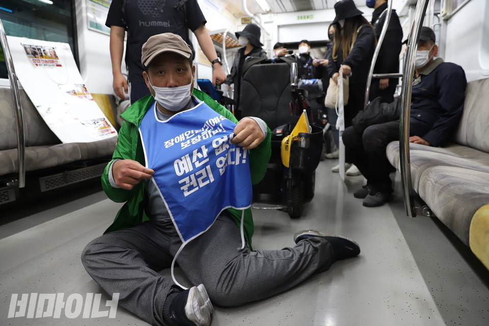 기자가 카메라를 들이밀자 오체투지 중인 장애인 활동가가 “장애인권리예산 보장하라! 예산 없이 권리 없다!”라고 적힌 몸피켓을 펼쳐 보이고 있다. 사진 강혜민