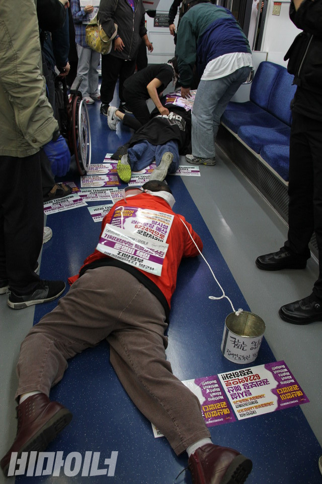 기자회견 직후 박경석 전장연 대표와 이형숙 서울시협의회 회장은 휠체어에서 내려 맨몸으로 지하철 바닥을 기었다. 그들의 목에는 장애인권리예산 보장을 촉구하는 글이 쓰인 깡통이 걸려 있다. 사진 허현덕