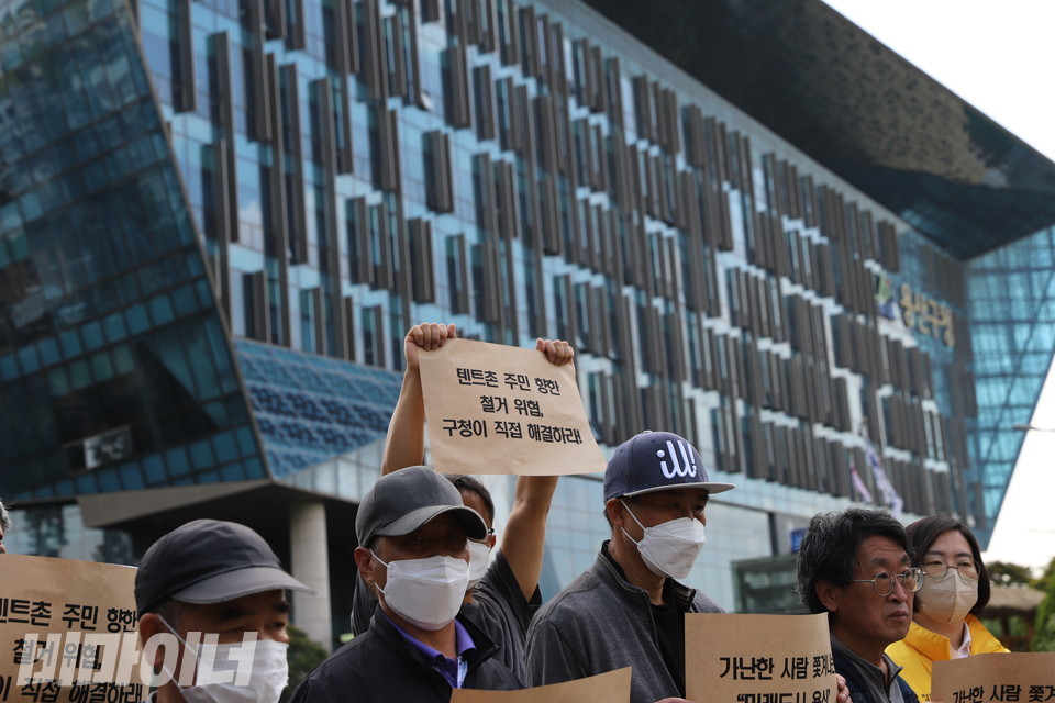 이동현 홈리스행동 상임활동가가 ‘텐트촌 주민 향한 철거 위협, 구청이 직접 해결하라’라고 적힌 피켓을 높이 들고 있다. 뒤에는 외부가 전면 유리로 된 용산구청 건물이 있다. 사진 하민지