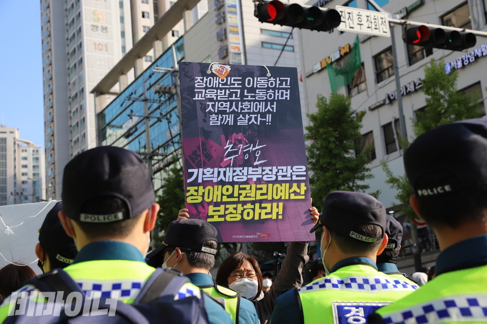 한티역 인근 횡단보도. 한 활동가가 경찰을 마주 본 채 피켓을 높이 들고 있다. 피켓에는 ‘장애인도 이동하고 교육받고 노동하며 지역사회에서 함께 살자! 추경호 기획재정부 장관(후보자)은 장애인권리예산 보장하라!’라고 적혀 있다. 사진 하민지