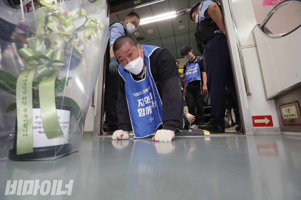 장애인 활동가가 “이동하고 교육받고 노동하고 지역사회 함께 살자”고 적힌 몸피켓을 입고 지하철 오체투지를 하고 있다. 그의 앞엔 윤석열 대통령 취임을 축하하는 난이 놓여 있다. 사진 강혜민