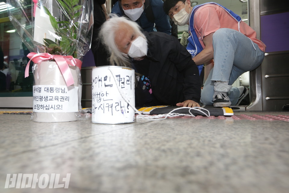 활동가의 지원을 받으며 오체투지를 하는 박경석 대표. 그의 앞에 윤석열 대통령 취임을 축하하는 화분과 “장애인권리법안 통과시켜라”라고 적힌 빈 깡통이 놓여 있다. 사진 강혜민