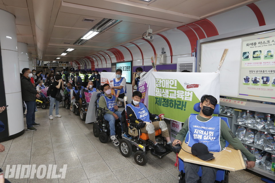 여의도역에서 엘리베이터를 기다리는 사람들의 긴 줄. 그 옆으로 “장애인평생교육법 제정하라”고 적힌 현수막이 펼쳐져 있다. 사진 이슬하