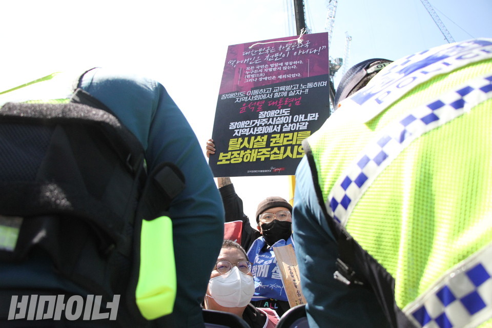 경찰들 넘어 한 활동가가 “윤석열 대통령님 장애인도 장애인거주시설이 아니라 지역사회에서 살아갈 탈시설 권리를 보장해주십시오”라고 적힌 피켓을 하늘 높이 들고 있다. 사진 이슬하 