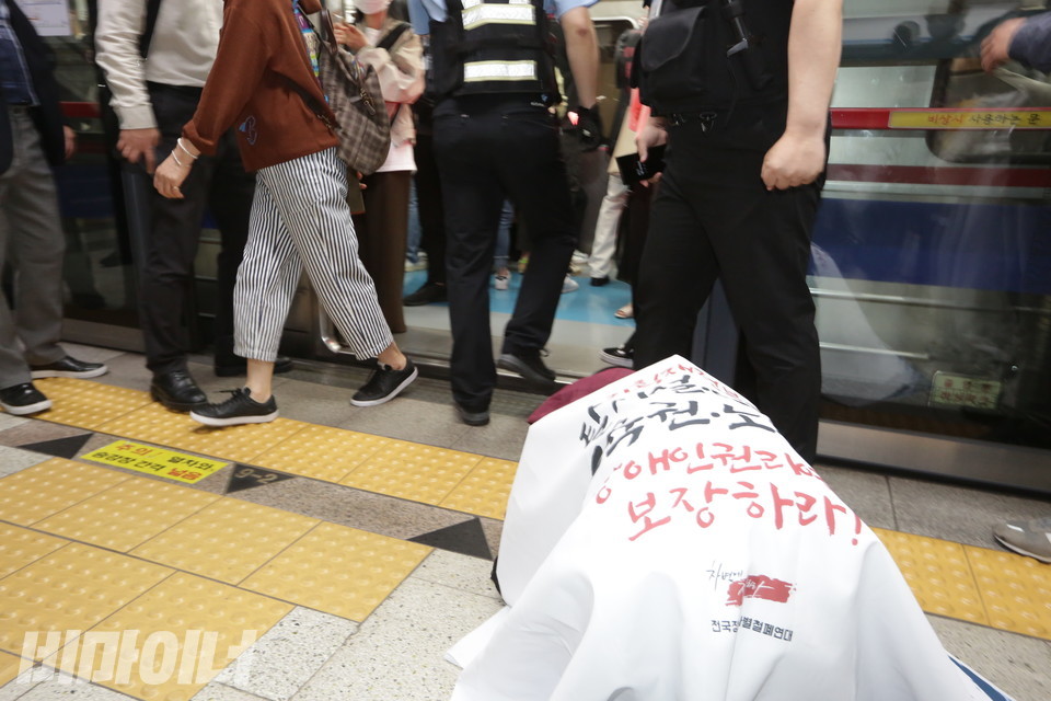 지하철 승강장에서 천을 두른 채 엎드려 있는 이상진 노동자 앞으로 승객 한 명이 내리고 있다. 사진 이슬하
