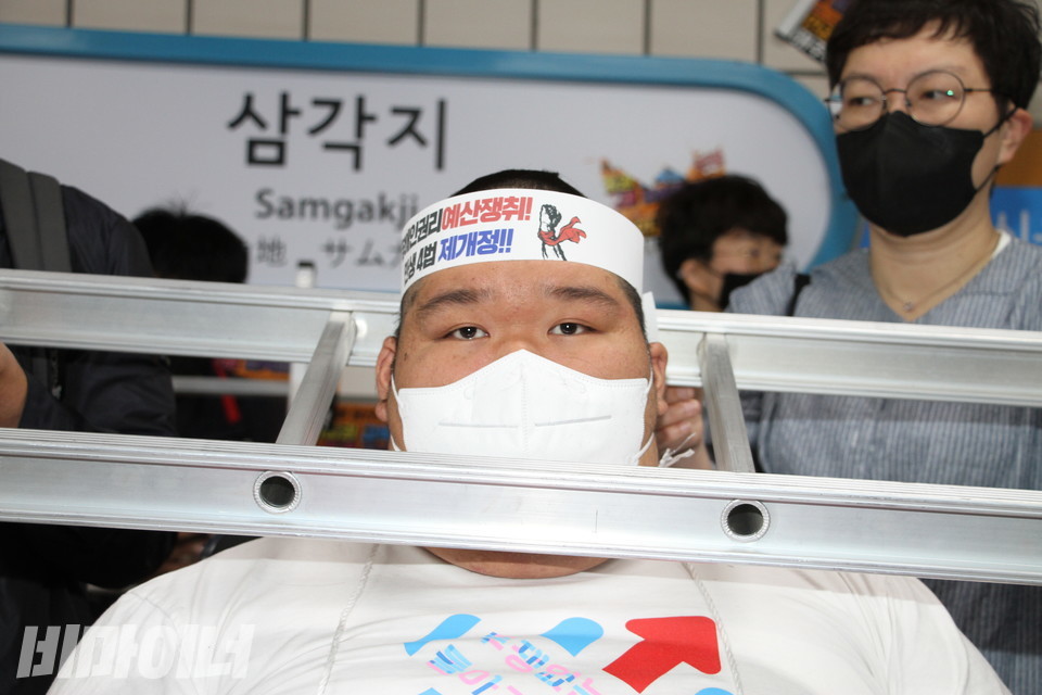 삭발을 마친 김대광 활동가가 사다리를 목에 건 채 정면을 응시하고 있다. 사진 이슬하