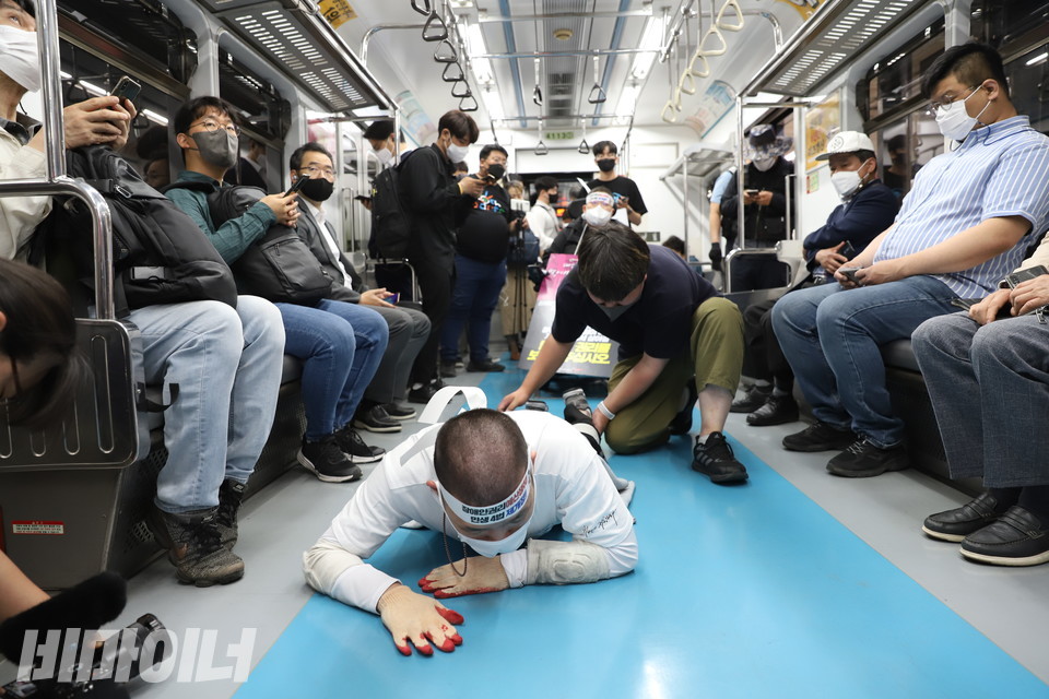 삭발한 이상도 활동가가 오체투지를 하고 있다. 그의 양옆에는 승객들이 의자에 앉아 있다. 사진 강혜민