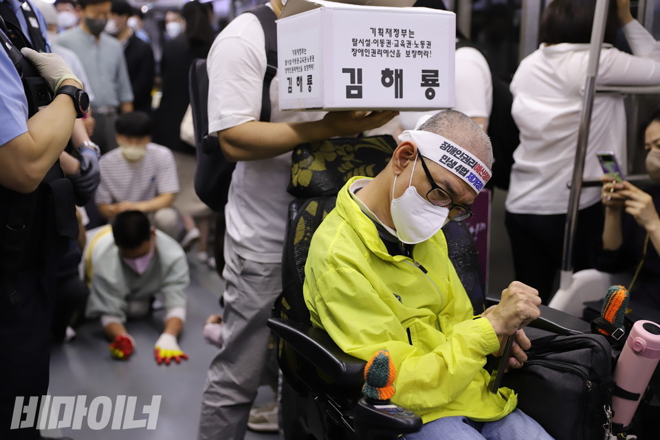 김해룡 동작장애인자립생활센터 소장이 지하철로 이동하고 있다. 뒤로 유진우 노들장애인자립생활센터 활동가가 오체투지를 하는 모습이 보인다. 사진 허현덕