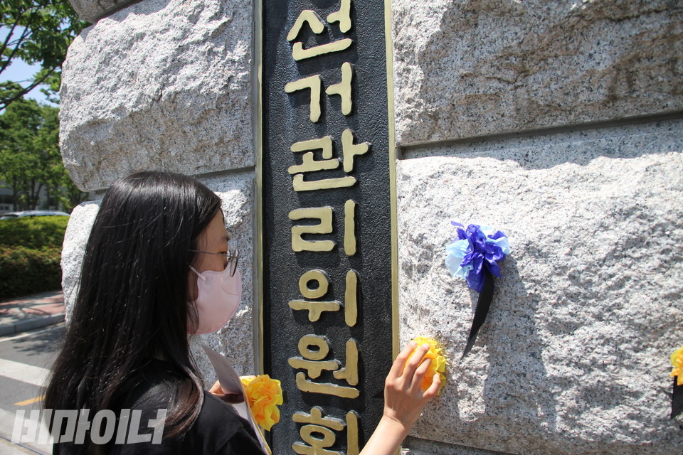 한 활동가가 중앙선관위 정문 벽면에 노란 꽃을 달고 있다. 사진 이슬하