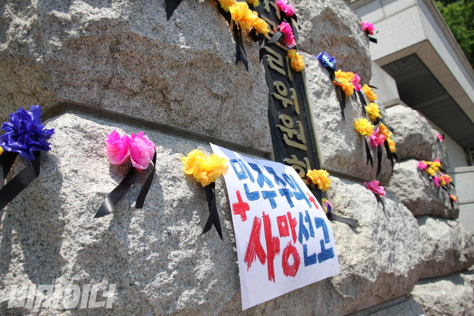 중앙선관위 정문 벽면에 활동가들이 단 꽃들과 “민주주의 사망선고”라 적힌 피켓이 붙어있다. 사진 이슬하