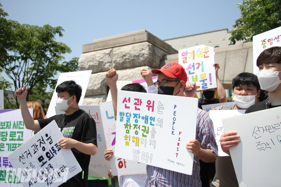 피켓을 든 기자회견 참가자들이 구호를 외치고 있다. 피켓에는 “선관위는 발달장애인의 참정권을 침해하지 말라”, “선거 과정을 (준비)하도록 모의투표, 사전설명회를 개최하라”, “알기 쉬운 선거 공보물” 등의 문구가 적혀 있다. 사진 이슬하