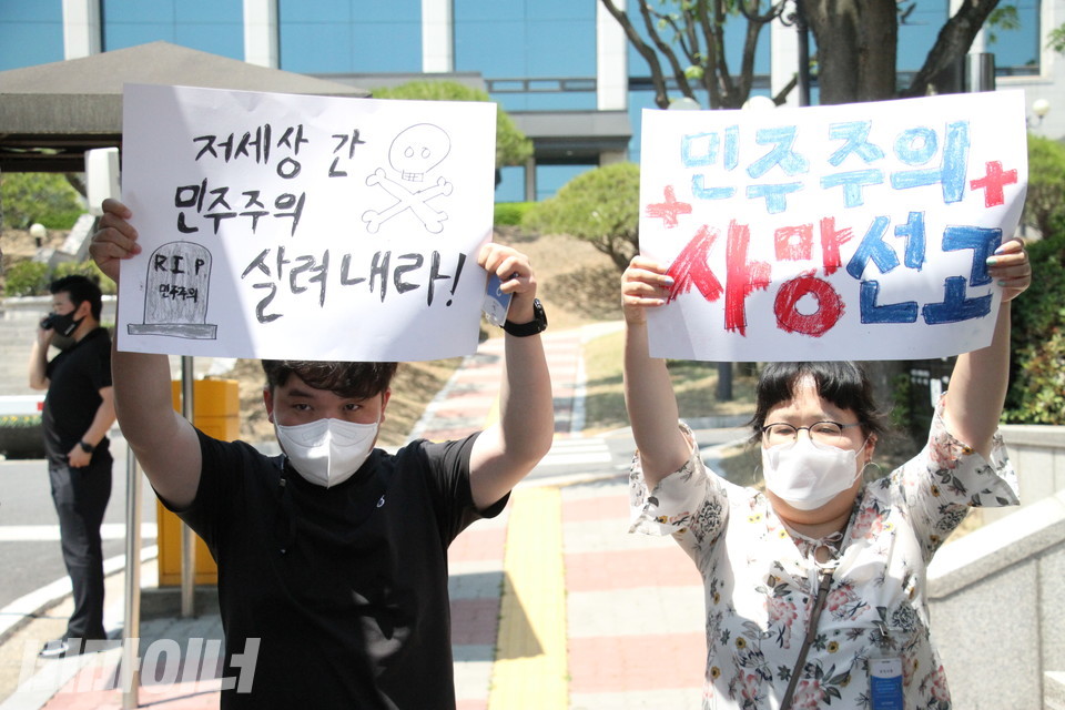 김대범 활동가와 문윤경 대표가 중앙선관위 정문 너머에서 피켓을 들고 있다. 피켓에는 “저세상 간 민주주의 살려내라”, “민주주의 사망선고”라고 적혀 있다. 사진 이슬하 