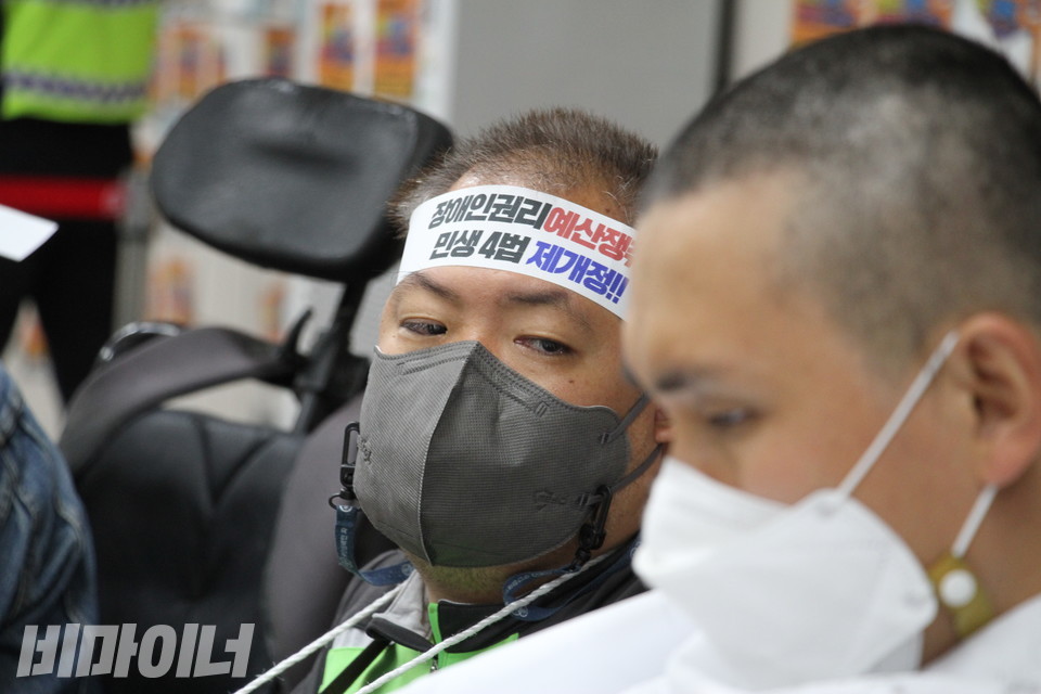 배재현 서울장애인차별철폐연대 대의원이 삭발한 김민석 진주장애인자립생활센터 소장을 바라보고 있다. 배 대의원의 머리띠에는 ‘장애인권리예산 쟁취, 민생4법 제개정!!’이라고 쓰여 있다. 사진 허현덕 