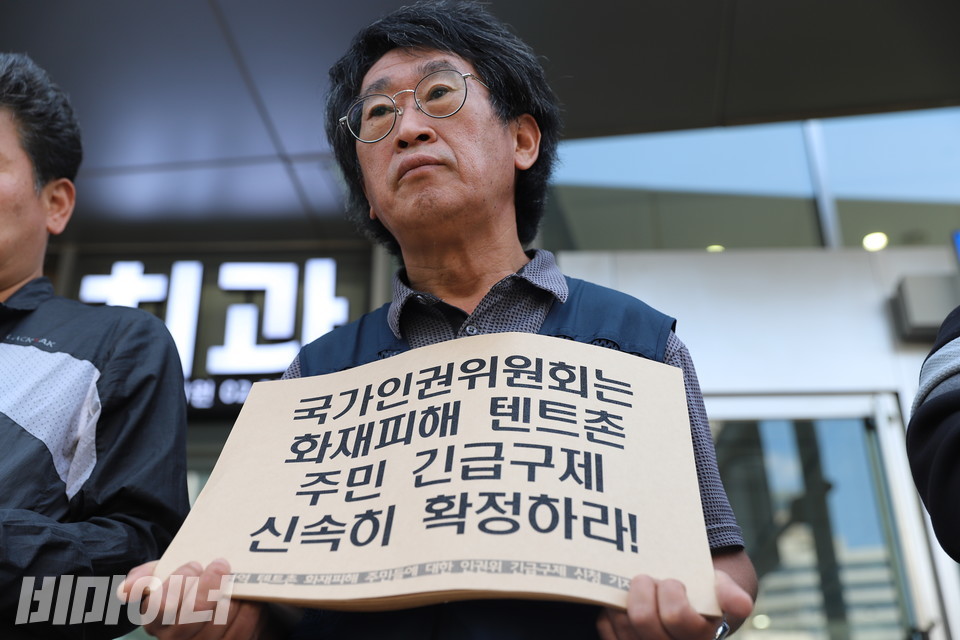 기자회견 참가자가 ‘국가인권위원회는 화재피해 텐트촌 주민 긴급구제 신속히 확정하라!’라고 적힌 피켓을 들고 있다. 사진 하민지