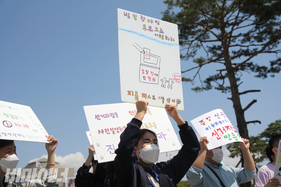 피플퍼스트서울센터 활동가가 “발달장애인 투표보조 이행하라”고 적힌 피켓을 들고 있다. 사진 이슬하