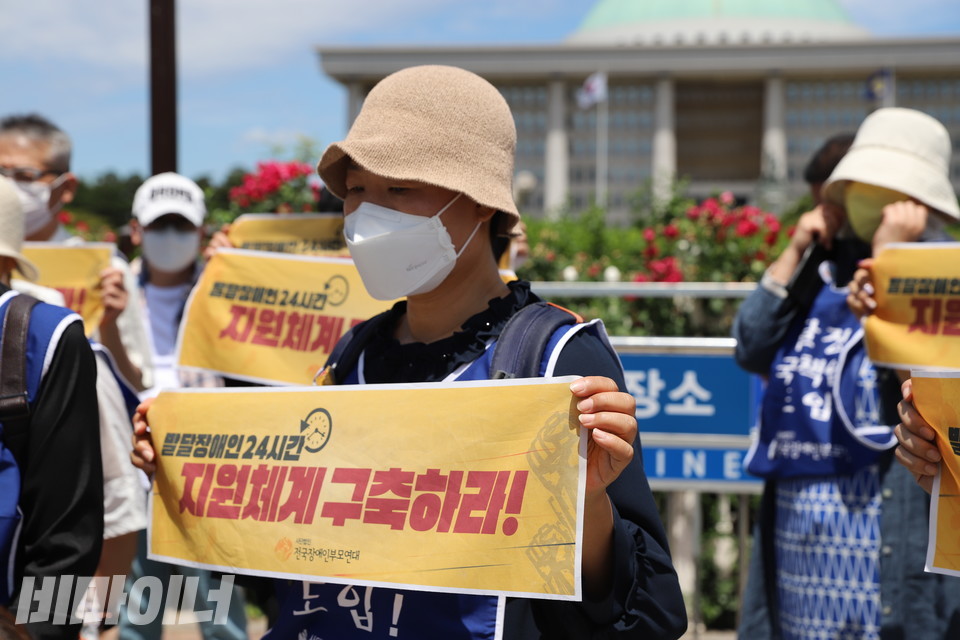 기자회견 참가자가 ‘발달장애인 24시간 지원체계 구축하라!’라는 손팻말을 들고 있다. 그의 표정이 어둡다. 사진 허현덕