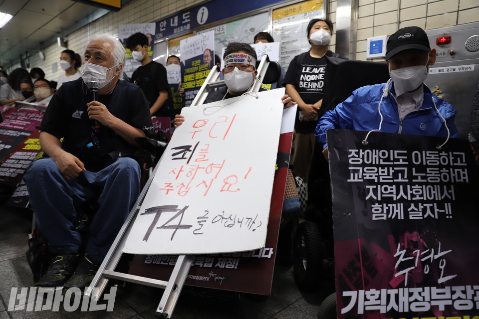 박경석 전장연 대표는 하얀 판넬에 “우리 죄를 사하여 주십시오! T4를 아십니까?”라는 문구를 써넣었다. 이형숙 회장이 판넬을 목에 걸고 있다. 사진 허현덕