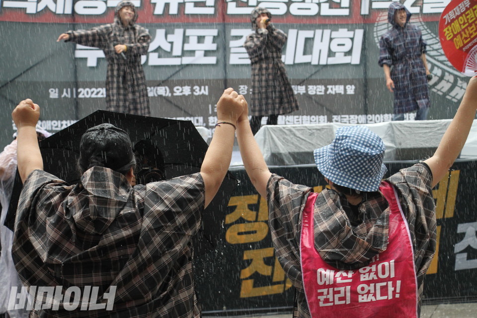 ‘노래로 물들다’ 공연을 보며 흥겨워하는 사람들. 장대비 속에서 두 사람이 손을 맞잡고 환호하고 있다. 등 뒤에는 “예산 없이 권리 없다!”는 문구가 적혀 있다. 사진 이슬하  