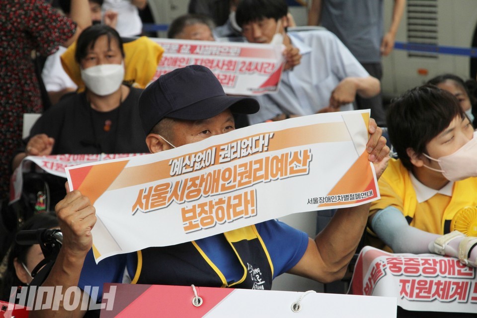 한 활동가가 ‘예산 없이 권리 없다! 서울시 장애인권리예산 보장하라! 서울장애인차별철폐연대’라고 적힌 작은 현수막을 들고 있다. 사진 하민지