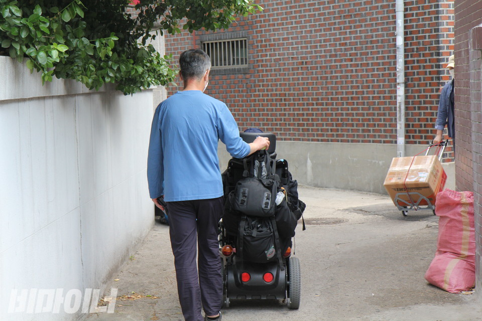 방 씨가 전동휠체어를 타고 골목길을 따라 집으로 향하고 있다. 그의 뒤를 새로 구한 민간 활동지원사가 따르고 있다. 사진 이슬하 