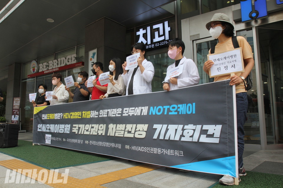 기자회견 참가자들이 현수막 뒤에 서 있다. 현수막에는 “연세오케이병원? HIV 감염인 차별하는 의료기관은 모두에게 NOT 오케이! 연세오케이병원 국가인권위 차별진정 기자회견”이라고 적혀 있다. 사진 이슬하