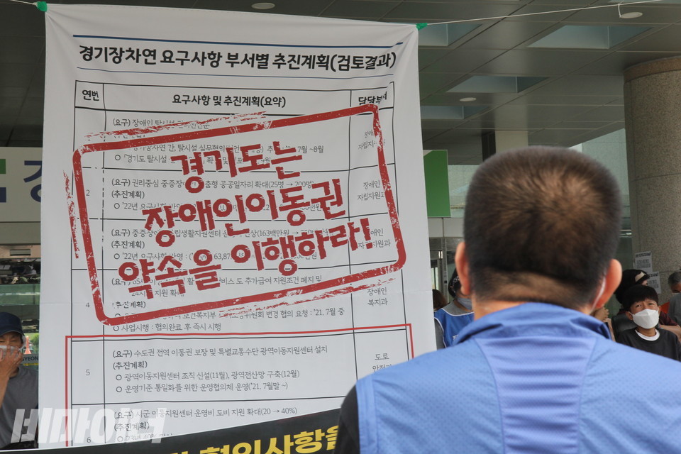 22일 오전 경기도청 북부청사 앞에서 열린 기자회견에서 권달주 경기장애인차별철폐연대 상임공동대표가 발언하고 있다. 그의 맞은편 청사 입구에 걸린 현수막에는 경기도가 보낸 ‘경기장차연 요구사항 부서별 추진계획(검토결과)’ 표가 보인다. 표 위에는 붉은 글씨로 “경기도는 장애인 이동권 약속을 이행하라!”고 적혀 있다. 사진 이슬하