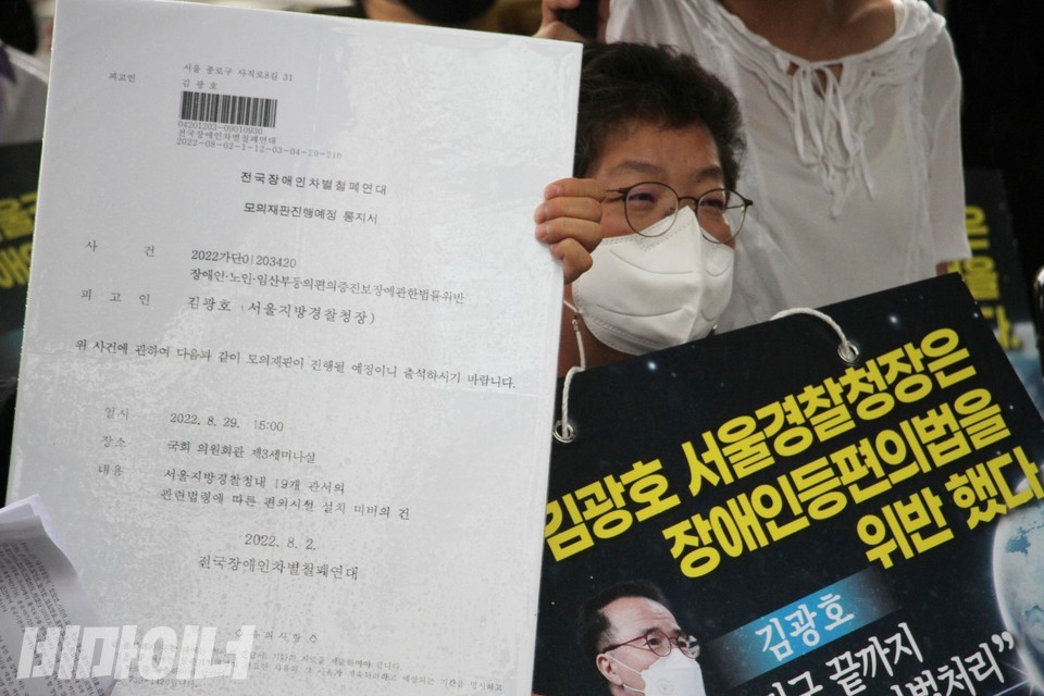 모의재판진행예정 통지서 피켓 옆에 이형숙 서울시장애인자립생활센터협의회 회장이 있다. 이 회장은 ‘김광호 서울경찰청장은 장애인등편의법을 위반했다’고 적힌 피켓을 들고 있다. 사진 하민지