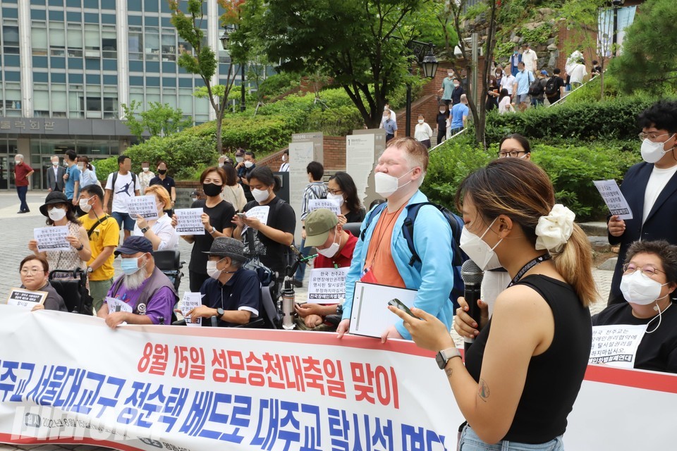 데레사라는 세례명을 가진 김수경 한국장애인자립생활센터협의회 활동가가 발언하고 있다. 기자회견 참가자들 너머로, 미사에 참여하려 명동성당으로 올라가는 신자들이 보인다. 사진 이슬하