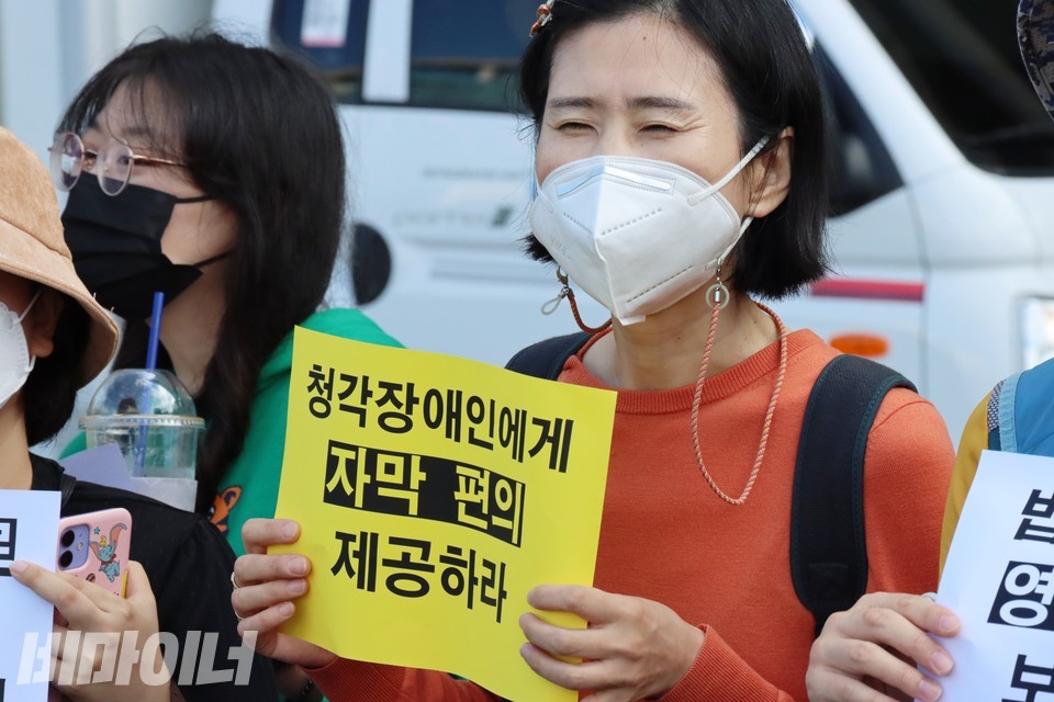 한 활동가가 ‘청각장애인에게 자막 편의 제공하라’라고 적힌 피켓을 들고 있다. 사진 하민지