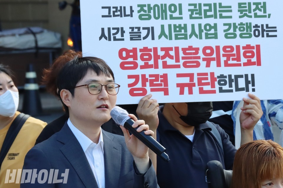 김재왕 변호사 뒤로 ‘그러나 장애인 권리는 뒷전, 시간 끌기 시범사업 강행하는 영화진흥위원회 강력 규탄한다’라고 적힌 피켓이 보인다. 사진 하민지