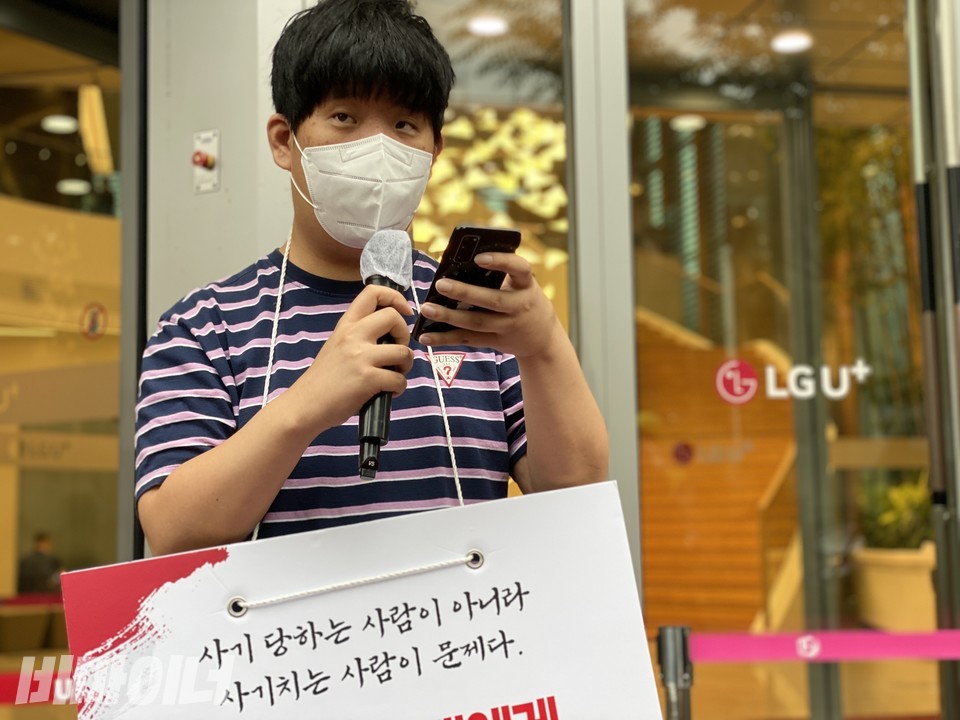 지난해 9월 7일, 김동호 활동가가 용산에 있는 LG유플러스 본사 앞에서 발언하고 있다. 그의 목에 걸린 피켓에는 “사기당하는 사람이 아니라 사기 치는 사람이 문제다”라고 적혀있다. 사진 비마이너DB