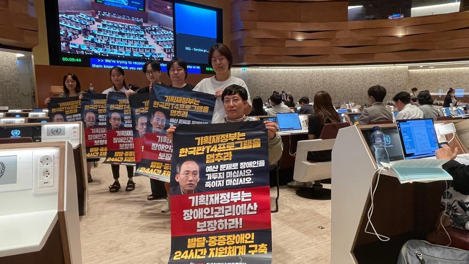 한국 심의가 열린 스위스 제네바 유엔 사무소 현장. 장애계연대 활동가 여러 명이 추경호 기획재정부 장관 사진이 있는 피켓을 들고 있다. 피켓에는 ‘기획재정부는 한국판 T4 프로그램을 멈추라. 예산 문제로 장애인을 가두지 마십시오. 죽이지 마십시오. 기획재정부는 장애인권리예산 보장하라! 발달·중증장애인 24시간 지원체계 구축’이라 적혀 있다. 사진 장애계연대