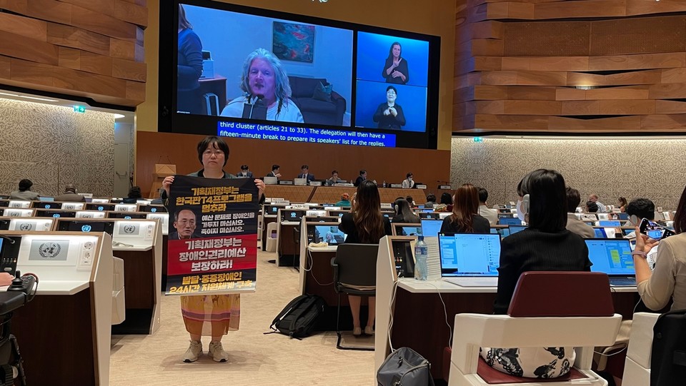 한국 심의가 열린 스위스 제네바 유엔 사무소 현장. 장애계연대 활동가가 추경호 기획재정부 장관 사진이 있는 피켓을 들고 있다. 피켓에는 ‘기획재정부는 한국판 T4 프로그램을 멈추라. 예산 문제로 장애인을 가두지 마십시오. 죽이지 마십시오. 기획재정부는 장애인권리예산 보장하라! 발달·중증장애인 24시간 지원체계 구축’이라 적혀 있다. 사진 장애계연대