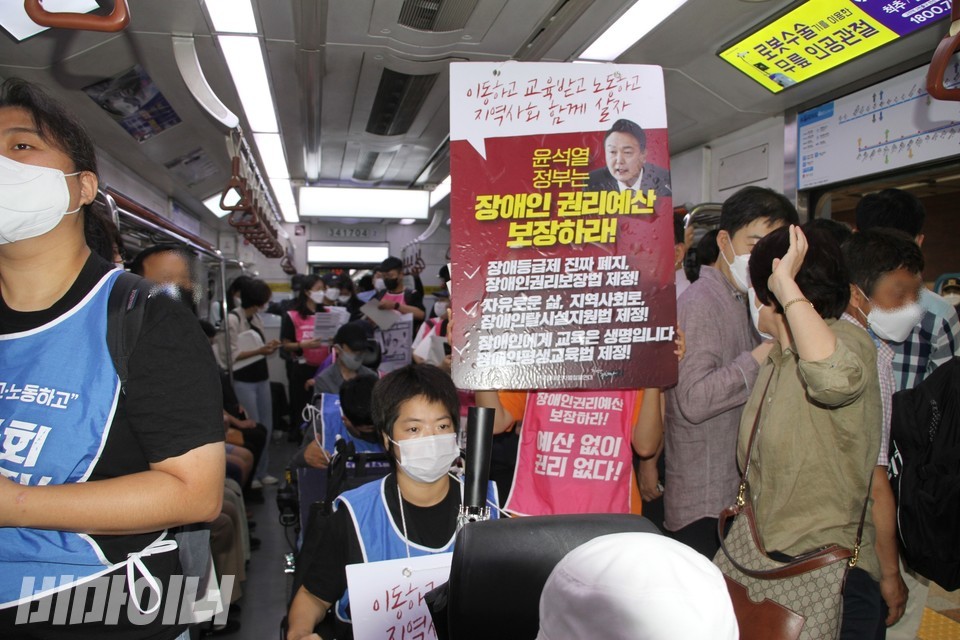 활동가들이 지하철 투쟁 중이다. 한 활동가가 윤석열 대통령 사진이 있는 피켓을 높이 들고 있다. 피켓에는 ‘이동하교 교육받고 노동하고 지역사회 함께 살자. 윤석열 정부는 장애인권리예산 보장하라!’라고 적혀 있다. 사진 하민지
