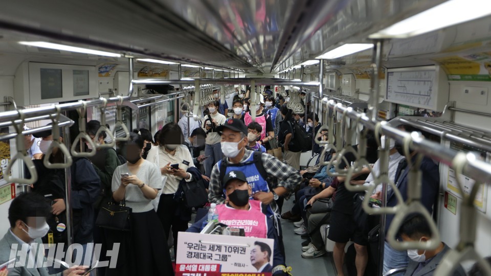 휠체어 행렬이 지하철 통로를 가득 메우고 있다. 좌우 승객들은 핸드폰만 바라볼 뿐, 무관심해 보인다. 사진 이슬하