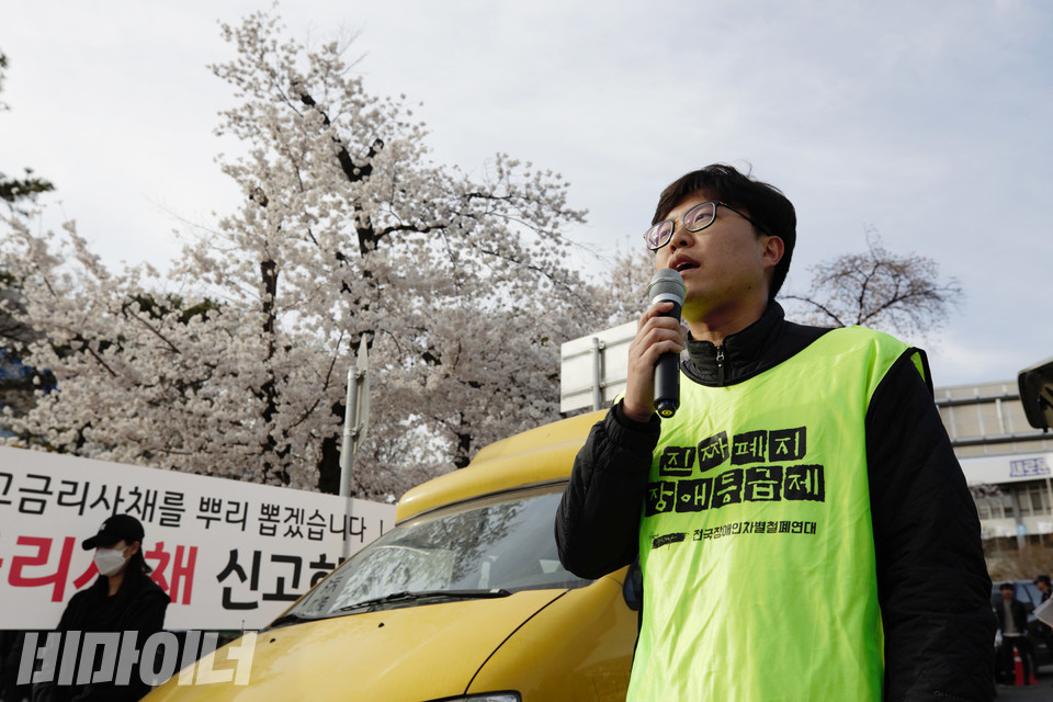2019년 4월 5일, 경기420장애인차별철폐공동투쟁단이 장애인거주시설폐쇄법·조례 제정을 촉구하며 경기도청 앞에서 전국집중결의대회를 열었다. 당시 대구시립희망원대책위 공동집행위원장으로 활동한 조민제 활동가가 “장애등급제 진짜 폐지”라고 적힌 몸자보를 입고 발언하고 있다. 사진 비마이너DB