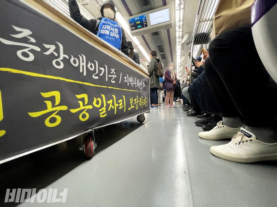 ‘중증장애인 기준 지역사회변화, 공공일자리 보장하라’라고 적힌 가짜 관 맞은 편에 비장애 승객의 발이 보인다. 사진 하민지